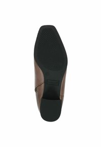 Hnědá kožená bota s texturovanou černou gumovou podrážkou. Má nízký podpatek a boční prošívání. Logo značky viditelné na podrážce.