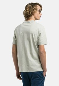 T-shirt in cotone grigio chiaro con maniche corte, scollo rotondo e vestibilità rilassata, mostrato da dietro. Texture liscia, design minimale.