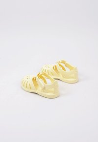 Yellow plastic sandals with multiple cutouts, open design, and adjustable back strap. Features logo on side and textured sole.