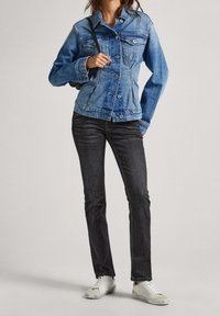 Jasnoniebieska kurtka dżinsowa z zapięciem na guziki, dwoma kieszeniami na piersi i dopasowanym krojem, zestawiona z ciemnymi dżinsami i białymi sneakersami.