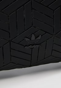 Svarta Adidas-skor med ett strukturerat mönster i fiskbensdesign. Logotypen är tydligt synlig i svart.