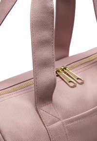 Vaaleanpunaiset kangaskahvat kiinnitetty laukun runkoon, jossa on kaksoiskultaiset vetoketjivetimet ylhäällä, näyttäen tekstuurimateriaalin ja ompeluyksityiskohdat.