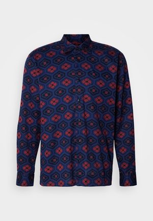 Langærmet skjorte i marineblå med hexagonale mønstre. Har røde blomsterdetaljer og sorte kanter. Knapkrave og stolpelukning.