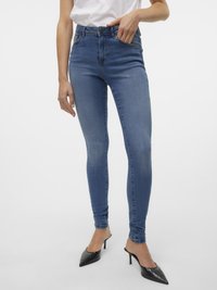 Tynne jeans i medium blå denim, med høy midje, beltestropper, fem lommer og lett falming. Kombinert med svarte spisse mules.