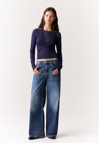Marineblaue Langarm-Wickelbluse, kombiniert mit lockeren, ausgebleichten blauen weit geschnittenen Jeans. Das Outfit besticht durch eine lässige Passform und einen weichen, leichten Stoff.