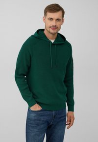 Groen hoodie met een textuur gebreid patroon, verstelbare trekkoorden en geribbelde manchetten, gedragen met blauwe jeans.
