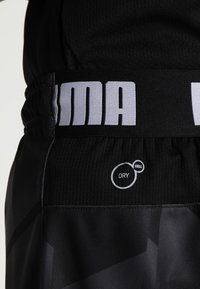 Svarta sportshorts med texturerad midja och vit "PUMA"-logotyp. Inkluderar "DRY CELL"-logotyp, vilket indikerar fuktavledande material.