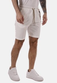Pantalones cortos blancos hechos de una tela ligera con una cinturilla elástica y cuerdas decorativas. Combinados con zapatillas blancas.