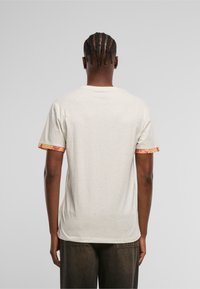 Camiseta de color crema con mangas cortas y un vibrante detalle estampado en los puños. Textura suave con sutiles motas a lo largo de toda la prenda.