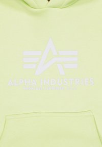 Felpa verde chiaro con un logo bianco che presenta lettere e linee stilizzate. Include una tasca frontale e una texture in tessuto morbido.