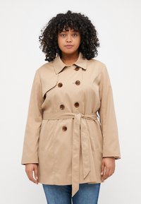 Beige trench coat med belted midje, dubbelknäppt knappstängning och sidofickor, med en klassisk krage och slät yta.