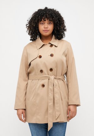 Trench-coat beige avec une taille cintrée à ceinture, fermeture à double boutonnage et poches latérales, présentant un col classique et une texture lisse.