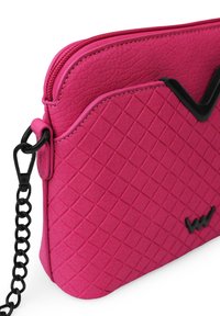 Pink crossbody bag in textured material, featuring a diamond pattern, a zipped closure, and a black chain strap with a contrasting accent.