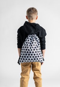 Widok z tyłu dziecka ubranego w czarną bluzę z kapturem, z torbą na sznurku z heksagonalnym wzorem w czerni i bieli.