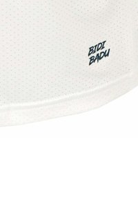 Weißes Hemd mit strukturiertem Oberflächen, versehen mit kleinen, gleichmäßig verteilten Punkten. Der Markenname "BIDI BADU" ist in einer marineblauen, kursiven Schrift gedruckt.