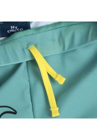 Turquoise stof met een gladde textuur heeft een gele trekkoord en een zwart bedrukt ontwerp. Het label leest "My Chicco."