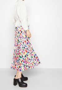 Falda midi plisada multicolor con una blusa blanca de corte holgado. Mules negros de plataforma con tacón cuadrado completan el atuendo.