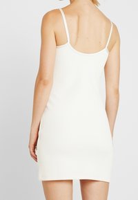 Abito aderente a coste in bianco con spalline sottili, schiena a scooper e orlo sopra la metà coscia. Il tessuto strutturato aggiunge interesse visivo.
