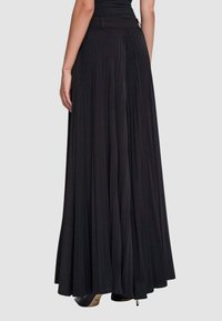 Gonna lunga nera plissettata con una fascia larga in vita e tessuto fluente. Presenta una zip nascosta sul retro e una texture liscia.