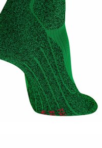 Primo piano di una calza lavorata a maglia verde e nera con testo rosso sulla punta, che mostra motivi testurizzati e dettagli di cucitura.