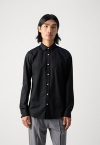 Schwarzes langärmliges Button-up-Shirt mit spitzem Kragen und kontrastierenden Knöpfen, das auf der Brust eine dezente Logo-Verzierung aufweist.