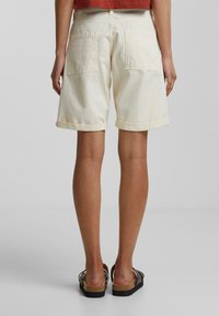 Shorts en crème clair avec une coupe décontractée, présentant des ourlets retroussés et deux grandes poches arrière, fabriqués en coton doux et texturé.
