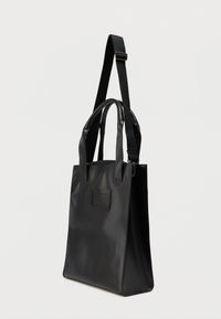 Μαύρη τσάντα χειρός με λεία, ματ επιφάνεια. Διαθέτει διπλές επάνω λαβές και ρυθμιζόμενο ιμάντα ώμου. Περιλαμβάνει μπροστινή τσέπη.