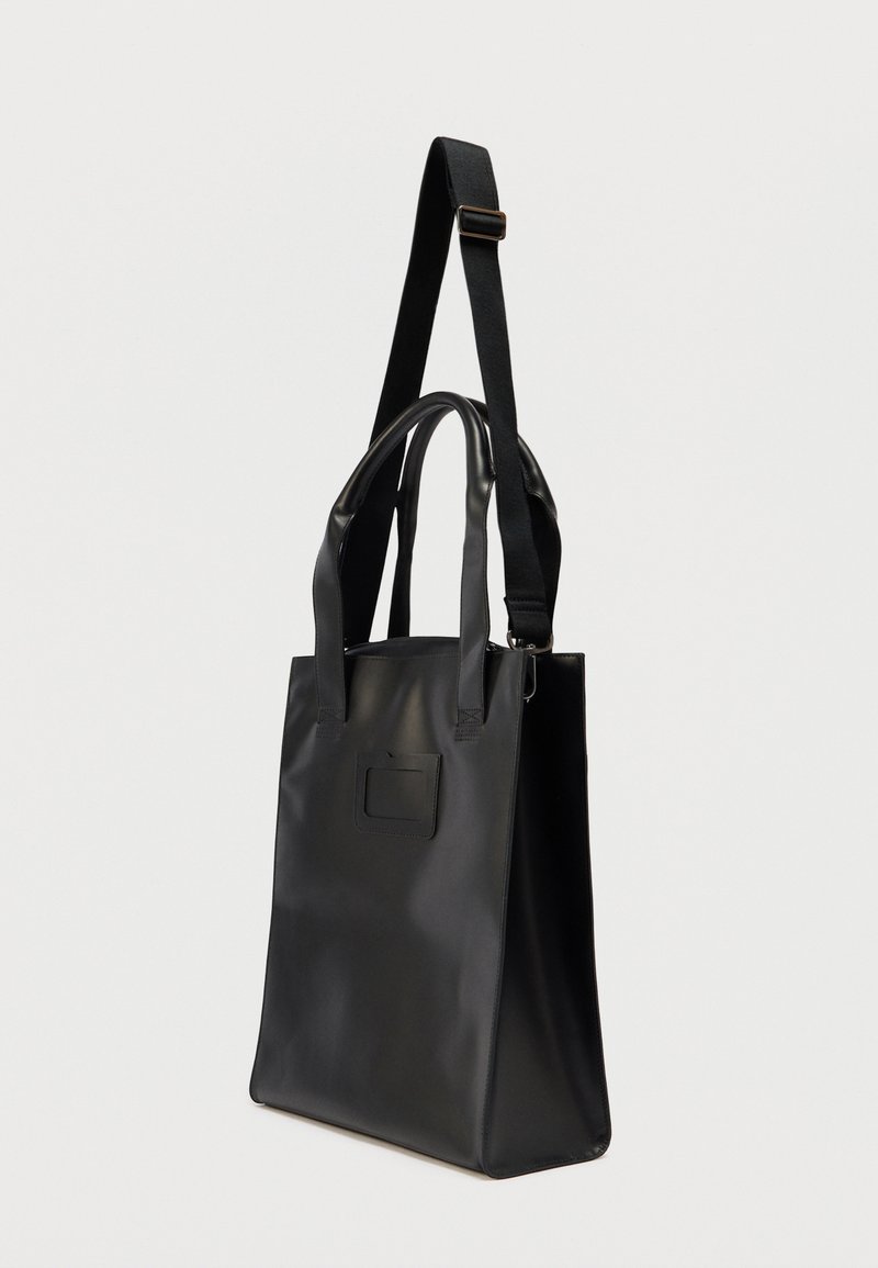 Zwarte draagtas met een gladde, matte afwerking. Voorzien van dubbele bovenhandvatten en een verstelbare schouderriem. Inclusief een voorvak met klep.