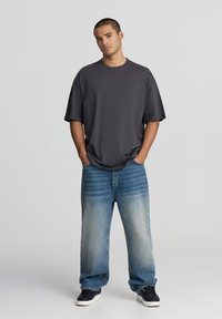 Czarnoszary, oversize t-shirt o luźnym kroju, zestawiony z jasnoniebieskimi spodniami o szerokich nogawkach z gradientowym wyblaknięciem. Czarne sneakersy dopełniają stylizację.