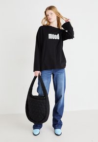 Crna majica dugih rukava s natpisom "mood" u bijeloj boji, uparena s plavim trapericama ravnog kroja i crnom prišivanom torbom za rame. Svijetloplave cipele.