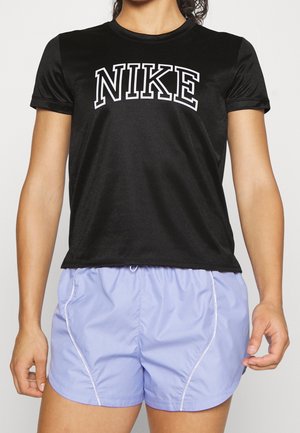 Persoon draagt een zwart Nike T-shirt met korte mouwen en lichtpaarse sportshorts, staat met de armen ontspannen langs het lichaam.