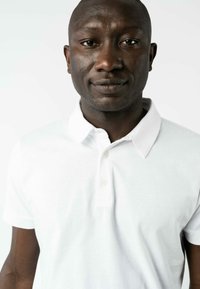 Weißes Baumwoll-Polohemd mit spitzem Kragen, kurzen Ärmeln und einer Knopfleiste mit drei Knöpfen. Glatte Textur, taillierte Passform, minimale Designdetails.