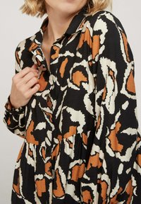 Robe à motifs floraux avec une palette de couleurs noire, blanche et orange. Comprend un col à boutons et des manches fluides avec un détail froncé.