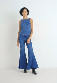 Denim odijelo s pripijenim, bezrukavim vrhom s bočnim vezicama i širokim trapericama. Tamnoplava boja s glatkom teksturom i klasičnim šavovima.