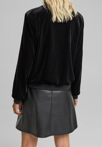 Czarna bomberka z aksamitu z ściągaczami przy mankietach i dole, zestawiona z czarną skórzaną mini spódnicą, gładka faktura i dopasowany krój.