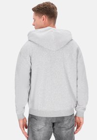 Sweat à capuche gris avec une capuche spacieuse, des poignets et un ourlet côtelés. Texture douce et coupe décontractée, associé à un jean gris. Vue de dos montrée.