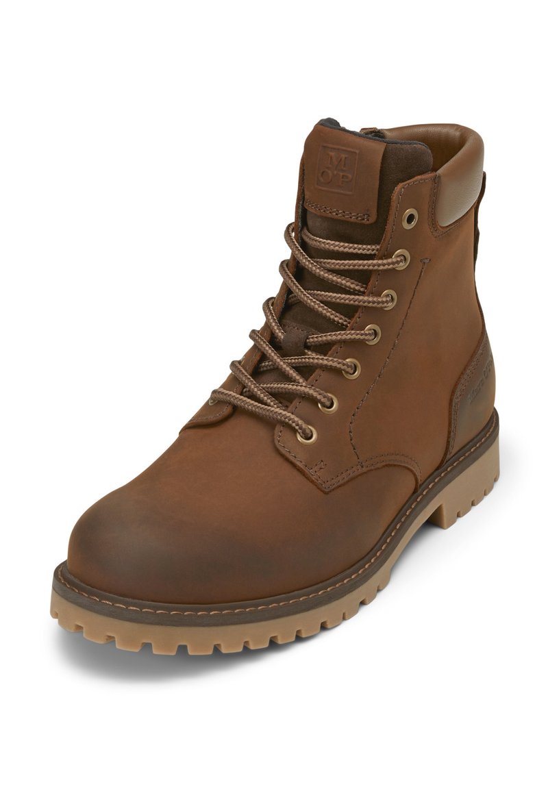 Bota de cuero marrón con cordones, punta redonda, ojales metálicos y suela de goma. Presenta un acolchado en el collar y un logo en relieve en el costado.