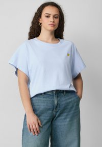 T-shirt en coton bleu clair à manches courtes, décolleté rond, présentant un petit détail brodé de fruit jaune sur le côté gauche.