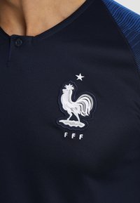 Tmavě modrý sportovní dres s bílým vyšitým logem kohouta a nápisem "FFF" pod ním, s kulatým výstřihem a texturovanými látkovými akcenty.