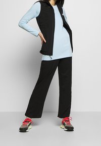 Musta hihaton liivi vaaleansinisen pitkähihainen paidan päällä, yhdistettynä mustiin housuihin ja värikkäisiin lenkkareihin. Varustettu taskuilla ja vetoketjuilla.