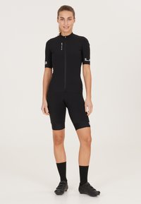 Svart cykeltröja med korta ärmar och dragkedja fram, ihop med svarta cykelshorts. Har varumärkets logotyp på ärmarna och elastiska nederkanter.