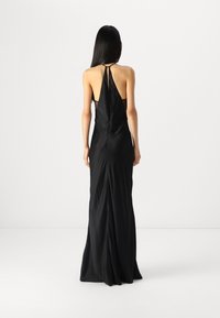 Black halter neck gown with a low back and flowing silhouette. Made of smooth fabric featuring a concealed zipper and minimal structure.