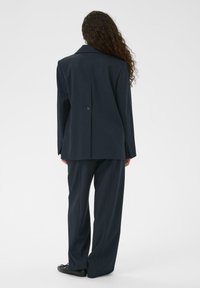 Marineblauer ma ßgeschneiderter Anzug mit einem langen Blazer mit Reverskragen und Vorderknöpfen, kombiniert mit weitem Hosenbein, gefertigt aus strukturiertem Stoff.