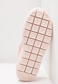 Die Sohle eines hellrosa Sneakers von unten betrachtet, mit einem strukturierten Muster aus Sternformen, glatten Rändern und einem Puma-Logo an der Ferse.