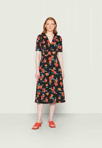 Vestido preto com flores e mangas curtas, apresentando padrões de flores vermelhas e azuis, decote em V e saia de comprimento médio. Combinado com sapatos slip-on vermelhos.