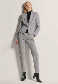 Grau maßgeschneiderter Anzug mit strukturiertem Finish, bestehend aus einem taillierten Blazer und schmalen Hosen. Kombiniert mit einem schwarzen Rollkragenpullover und schwarzen Stiefeletten.