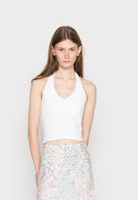 Top de alças brancas com um desenho em V, combinado com uma saia de padrão floral em cores pastel e um tecido leve.