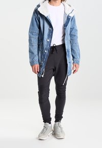 Denim jacket with a fleece-lined hood, light blue color, and snap buttons. Black tapered pants with texture detail and grey athletic shoes.