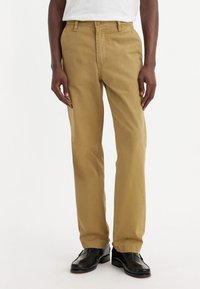Pantaloni din bumbac khaki, cu un design drept, av�ând un brâu și buzunare frontale, asociați cu pantofi eleganți negri.