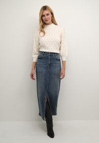 Pull en tricot crème à col montant et manches bouffantes, associé à une jupe en denim bleu mi-longue avec une fente avant et une texture décolorée.